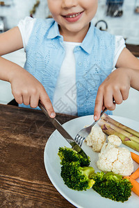 微笑的孩子用刀拿着叉子吃西兰花的镜头图片