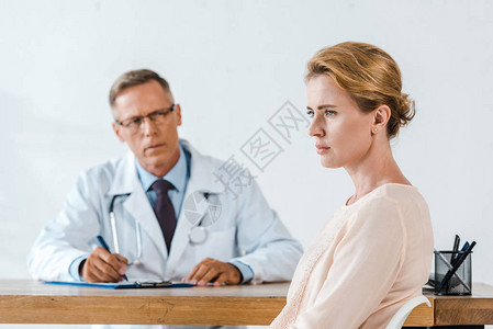 穿着白色大衣坐在医生旁边的不高兴的女图片