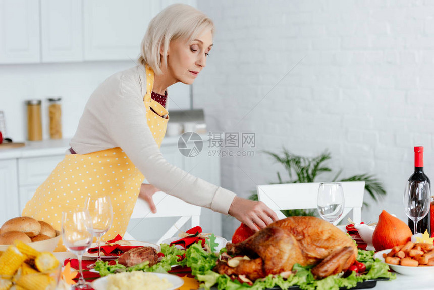 美丽的高级美女在厨房做感恩节晚宴的餐桌服务图片