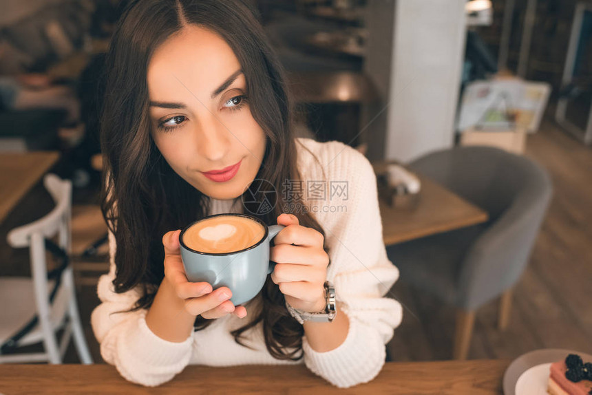 在咖啡馆餐桌上喝咖啡的有吸引力的年轻女子图片