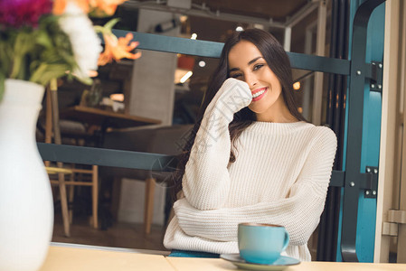 快乐而有吸引力的年轻女子在咖啡厅用咖啡杯坐背景图片