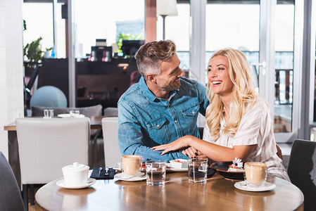 快乐的一对欢笑的情侣握着手在咖啡馆图片
