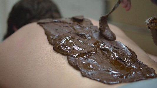 Spa沙龙的近身按摩治疗师在男背部涂抹棕色混合物SPA护理放松和治疗图片