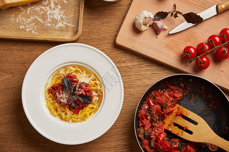 木桌上的意大利面盘和番茄酱煎锅的顶部视图图片