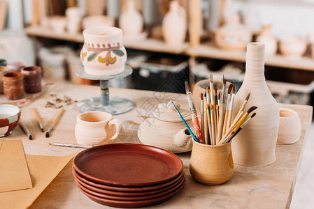 陶器车间木桌上的陶瓷餐具和刷子图片