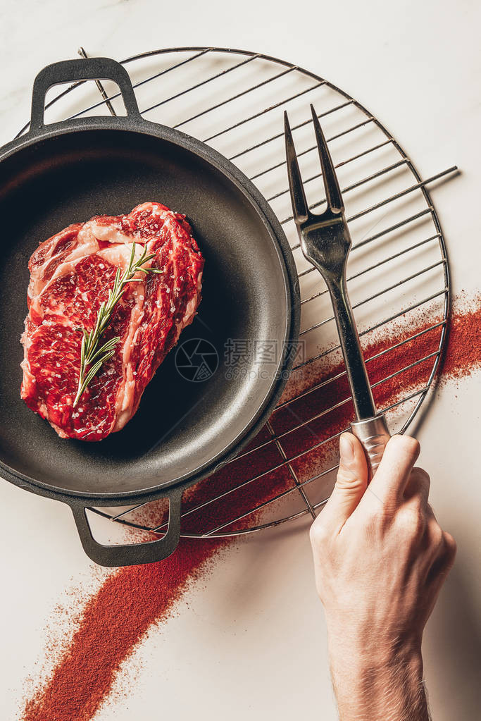 男人在厨房里拿着肉叉和餐牛排用迷迭香做图片