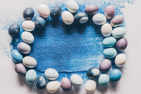 白色表面上彩绘复活节彩蛋和蓝沙的顶视图背景图片