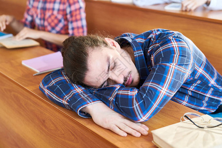 穿着校服躺在木桌边在大学讲课时睡觉的身着格式衬衫的英俊长臀图片