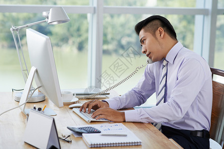 亚洲商人在办公室打电话时在电脑上工作图片