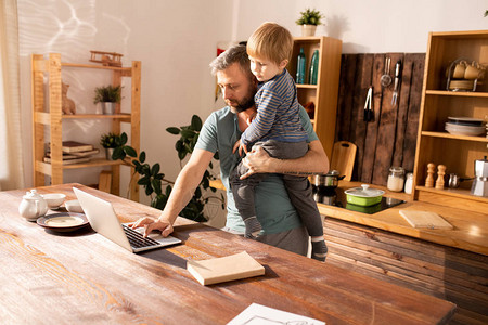 在家工作时持小儿子和打笔记本电脑的单身父亲图片