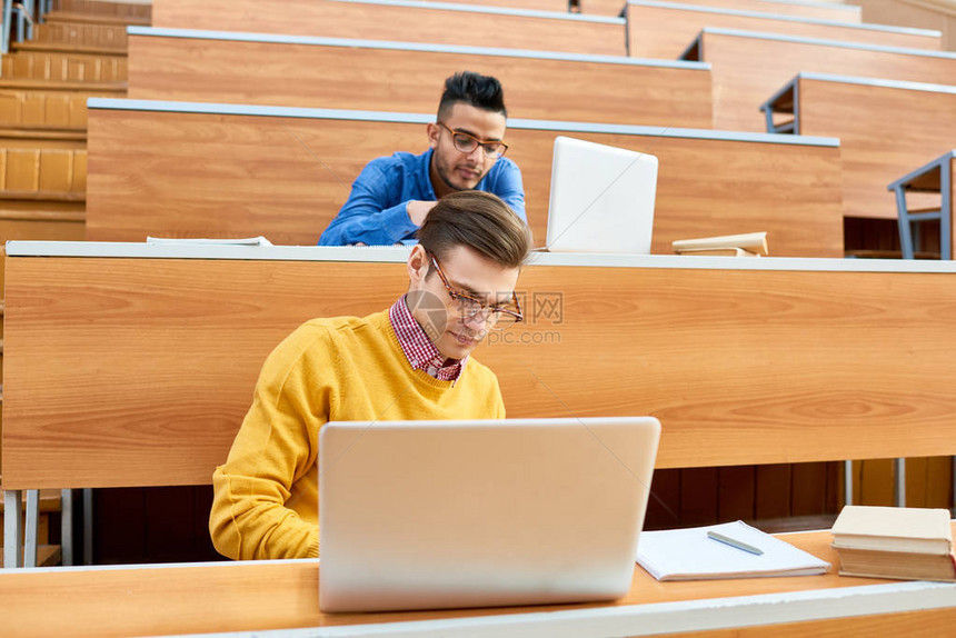 两名学生坐在大学陡峭礼堂的课桌前准备上课的肖像图片