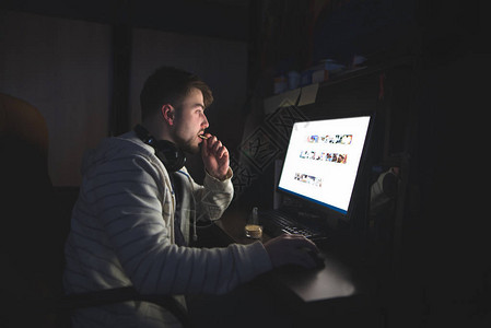 男人晚上坐在家里用电脑吃饼干图片