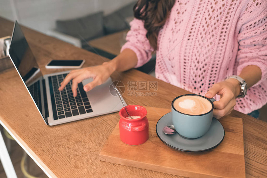 女自由职业者在咖啡厅用智能手机和咖啡杯坐在桌边时使用笔记本电图片