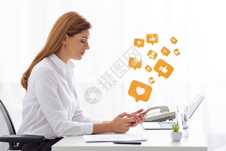 使用近文件和桌上笔记本电脑的智能手机的女商人侧面视图图片