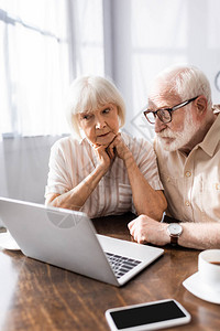 在智能手机和桌上咖啡附近看笔记本电脑的老年夫妇有图片
