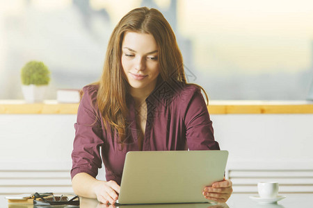 利用膝上型电脑在现代城市办公室的玻璃桌面上安装有吸引力的女士肖像背景图片