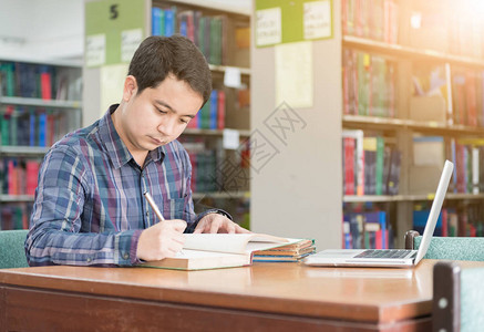 年轻学生在图书馆从一本书做笔记图片