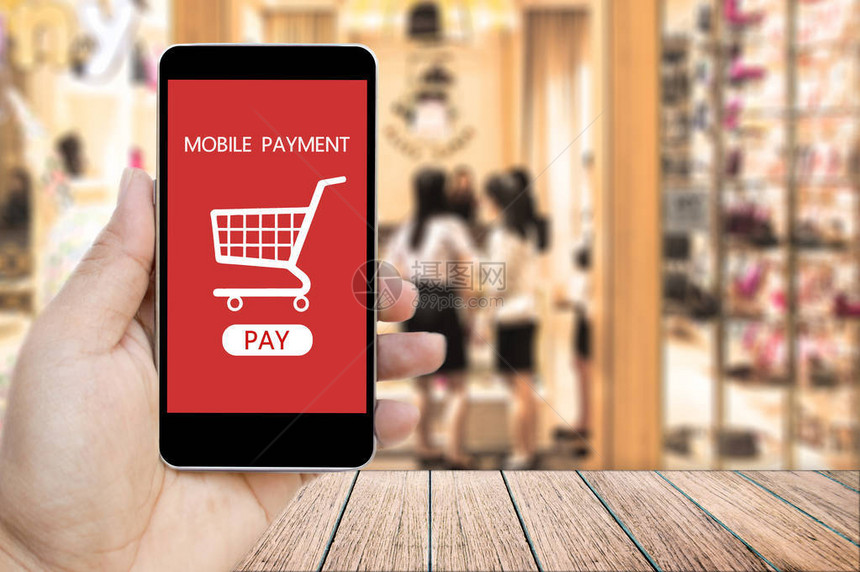 手持智能手机与移动支付和购物车在屏幕上模糊购物中心背景商业和金融图片