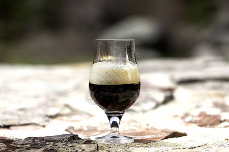 大自然石桌上的泡沫黑啤酒杯图片