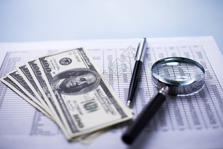 用放大镜笔和分析财务报告的粉红美元钞票的概念图象图片