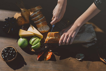 女人用落叶在桌子上切法棍面包的镜头图片