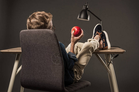 小男孩坐在桌子上用腿躺着将苹果放图片