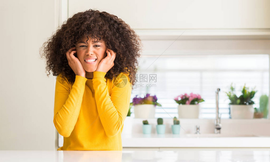 衣着黄色毛衣的非洲女在厨房用指头遮住耳朵图片