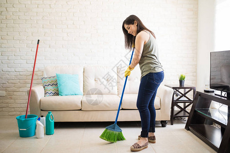 快乐的年轻女佣扫地板家里有绿色图片