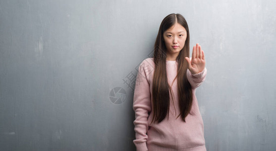 年轻的女人在灰色的墙上做停止用手掌唱歌脸上带着消极和严肃的图片