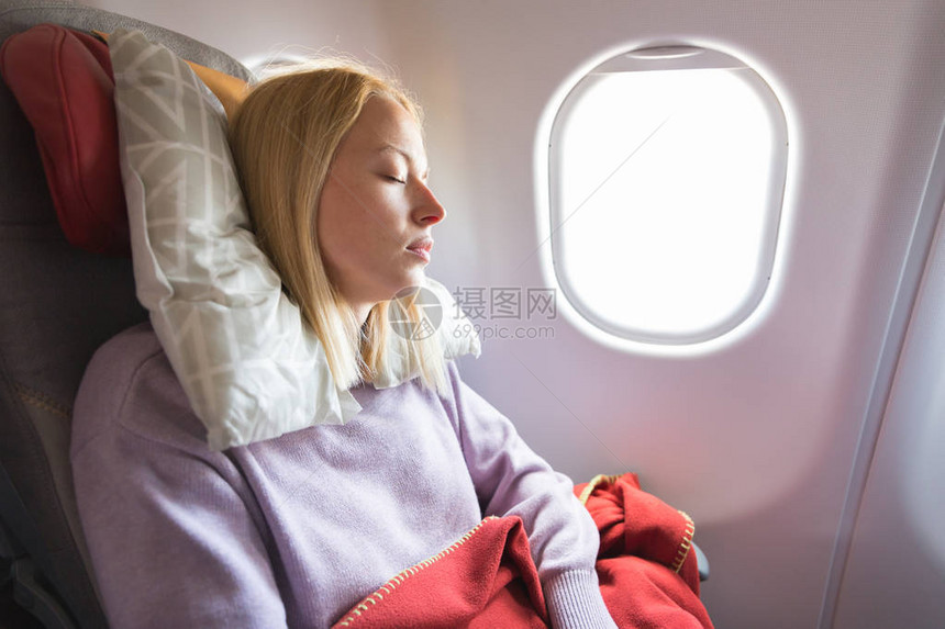疲惫的金发休闲白种女人在长途跨大西洋航班上睡在座位上通过飞机图片