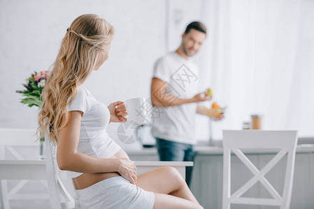 孕妇坐在椅子上喝茶丈夫站在厨房柜台图片
