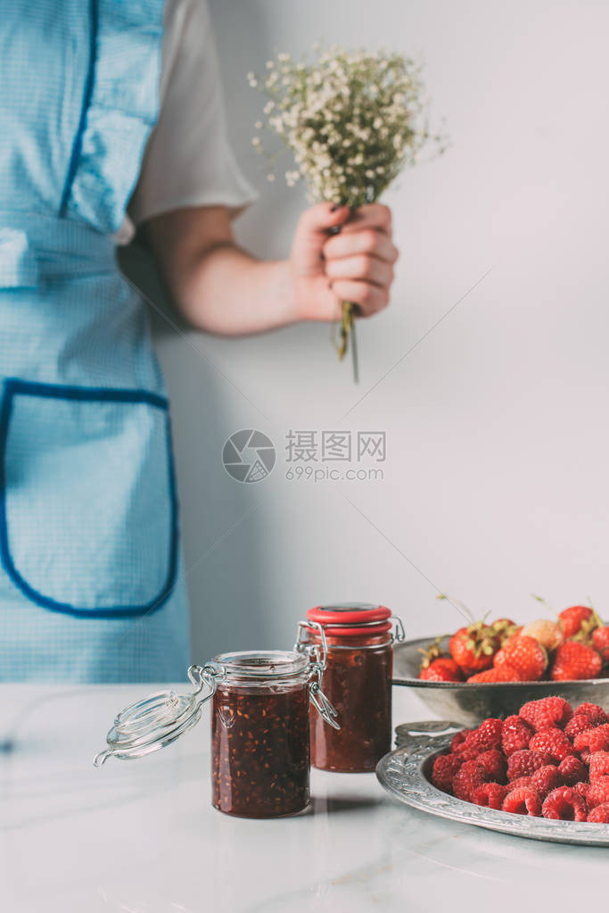 围裙上的妇女在桌边拿着鲜花草莓草莓和果酱罐头的花图片