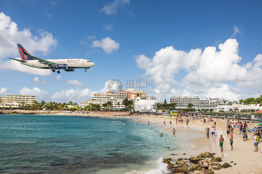 一架喷气式飞机在马霍海滩的旁观者上方接近朱莉安娜公主机场短跑道让海滩游客可以近图片