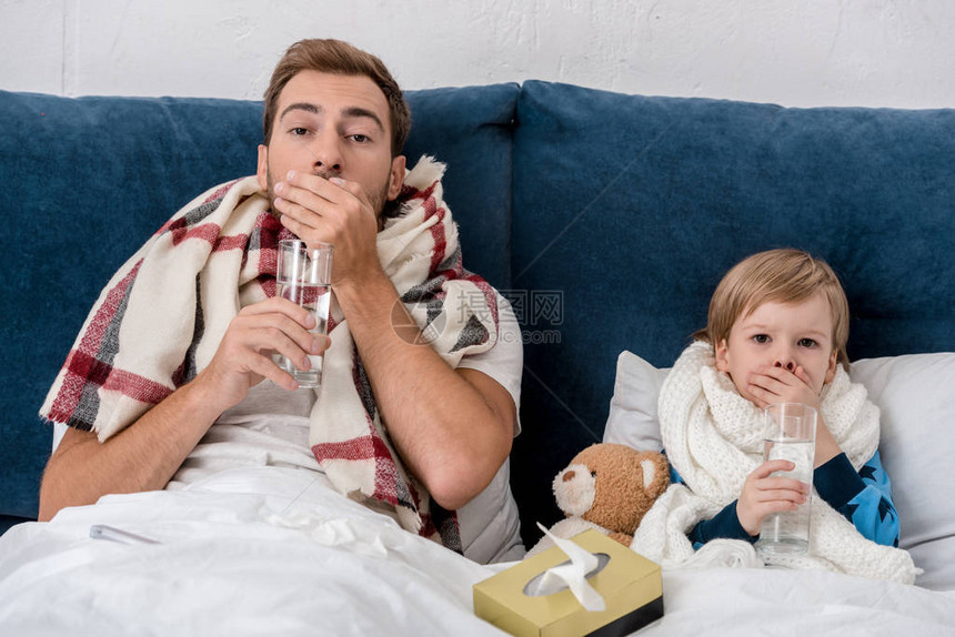 父亲和儿子生病在床上看照相机时用杯子图片