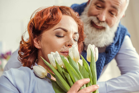 拥有郁金香花束花的成熟女和看着她的留胡子的男人图片