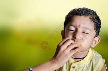 印度亚裔小男孩闭着眼睛吃甜食享受美味图片