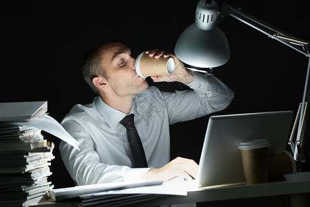 晚上在办公桌前喝咖啡的商人图片