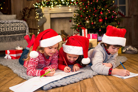 戴圣诞老人帽子的儿童在灰地毯上画图片