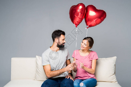 坐在白沙发上的一对微笑的情侣用红色心形气球图片