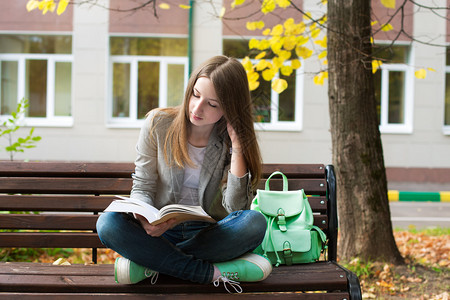 学生坐在长椅上在秋天看书图片