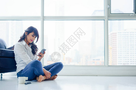 坐在地板上看手机的年轻女士图片