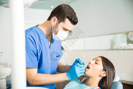 男牙医在诊所用牙镜和雕刻器检图片
