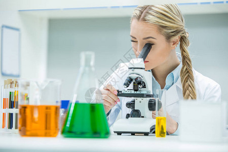 在化学实验室与显微镜合作的年轻女科学家图片