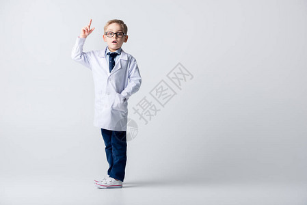 穿着医疗制服和眼镜的惊吓小男孩用指头举起图片