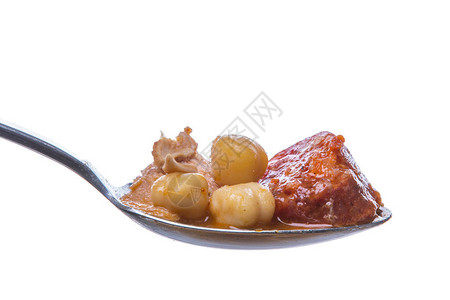 用鹰嘴豆和肉片在勺子上用白色隔开的炖肉的特写镜头图片