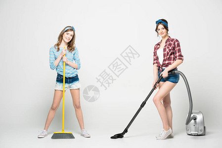 两个美丽的年轻女站在扫帚和吸尘清洁器的旁边微背景图片
