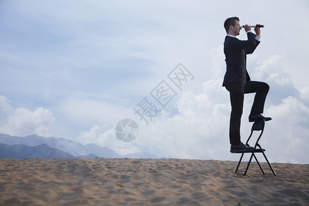 商人站在椅子上透过望远镜在沙漠中看图片