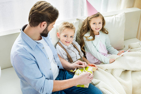 父亲和两个笑的孩子坐在沙发上给图片
