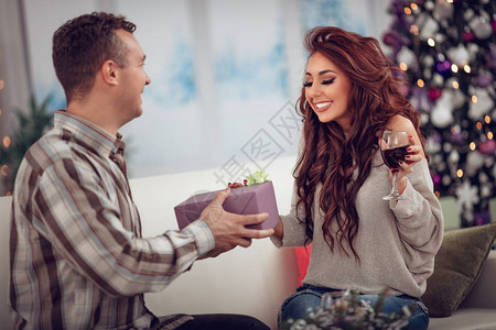 美丽的年轻夫妇在家庆祝圣诞节英俊的微笑男人正在给他漂亮的女朋图片