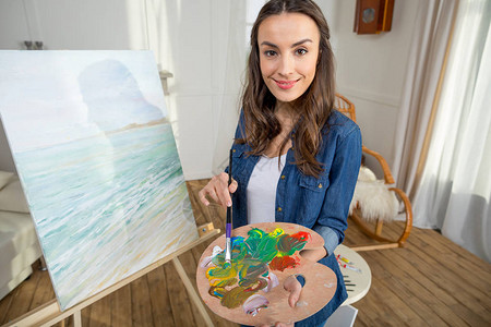 有魅力的年轻女艺术家带着画笔和调色板图片